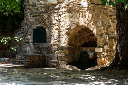 Free Ancient stone fountain set within a picturesque outdoor scene, surrounded by lush greenery. Stock Photo