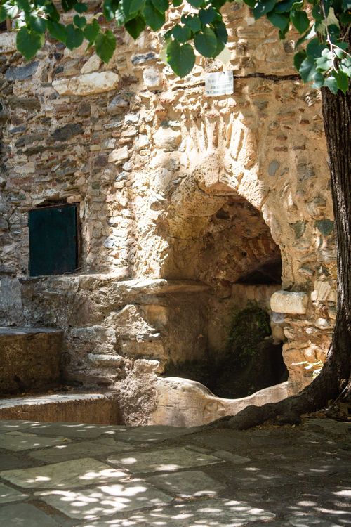 Free Sunlit stone archway and courtyard with rustic texture and leafy shadows. Stock Photo