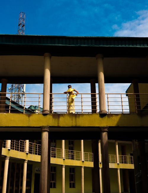 Free Fashionable woman in yellow stands on a modern balcony under bright blue sky, showcasing contemporary architecture. Stock Photo