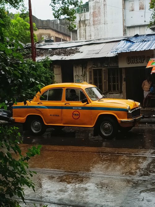 Free Vintage yellow taxi parked on a rainy street in Kolkata, India, capturing monsoon vibes. Stock Photo