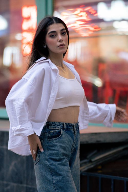 Free Stylish portrait of a young woman in casual attire, captured outdoors with vibrant city lights. Stock Photo