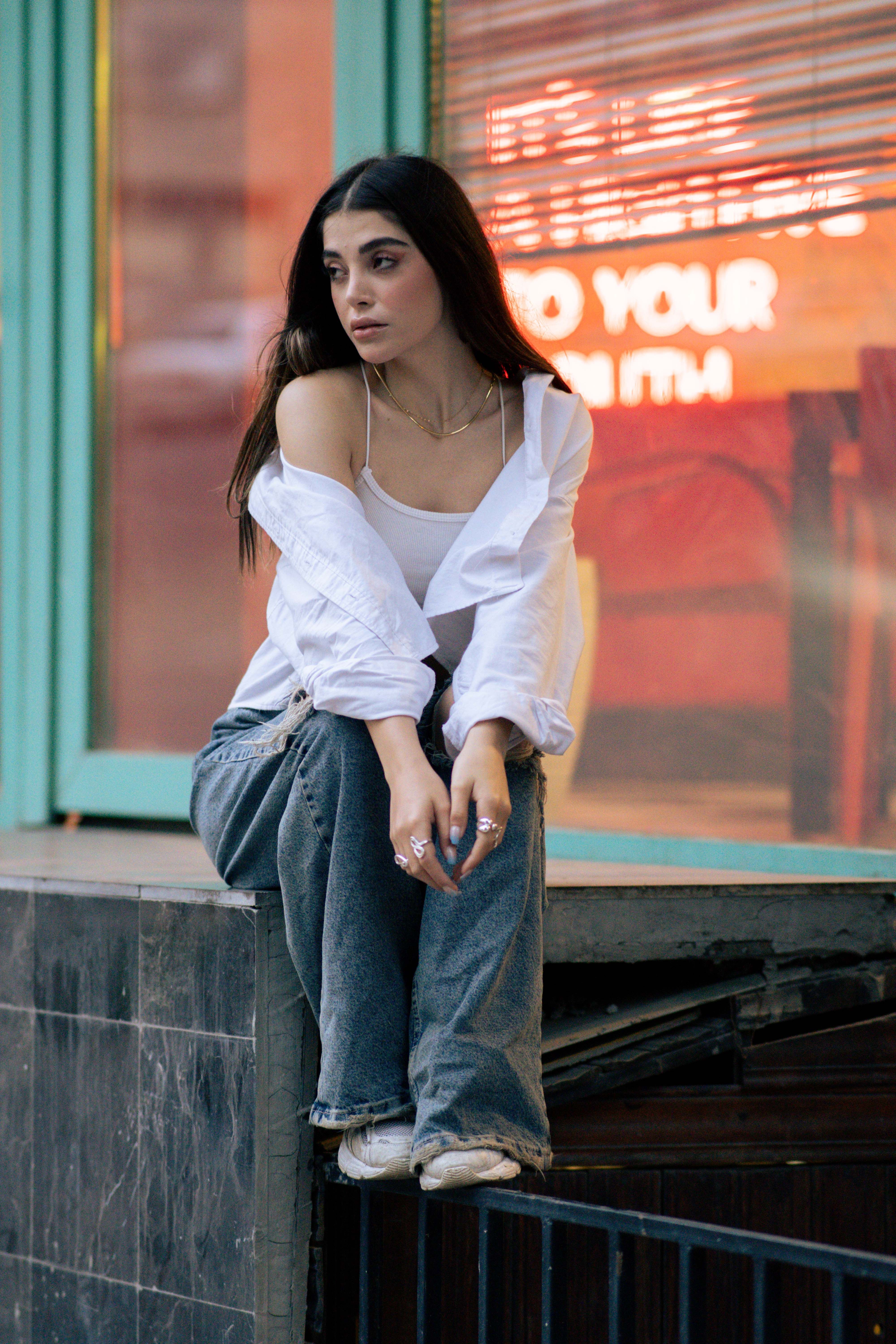 Stylish woman sitting against urban backdrop in Tehran, capturing modern fashion essence.