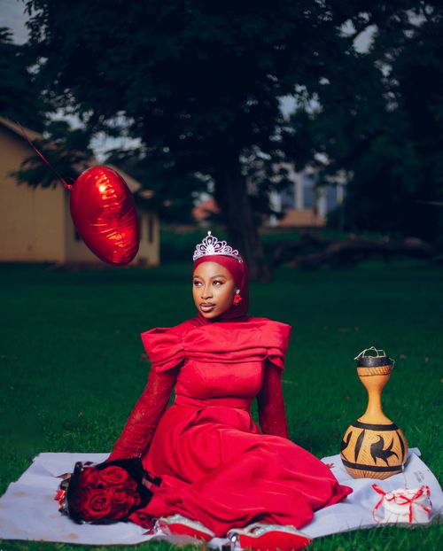 Free A woman in a red dress and tiara sits on grass with a heart balloon. Stock Photo