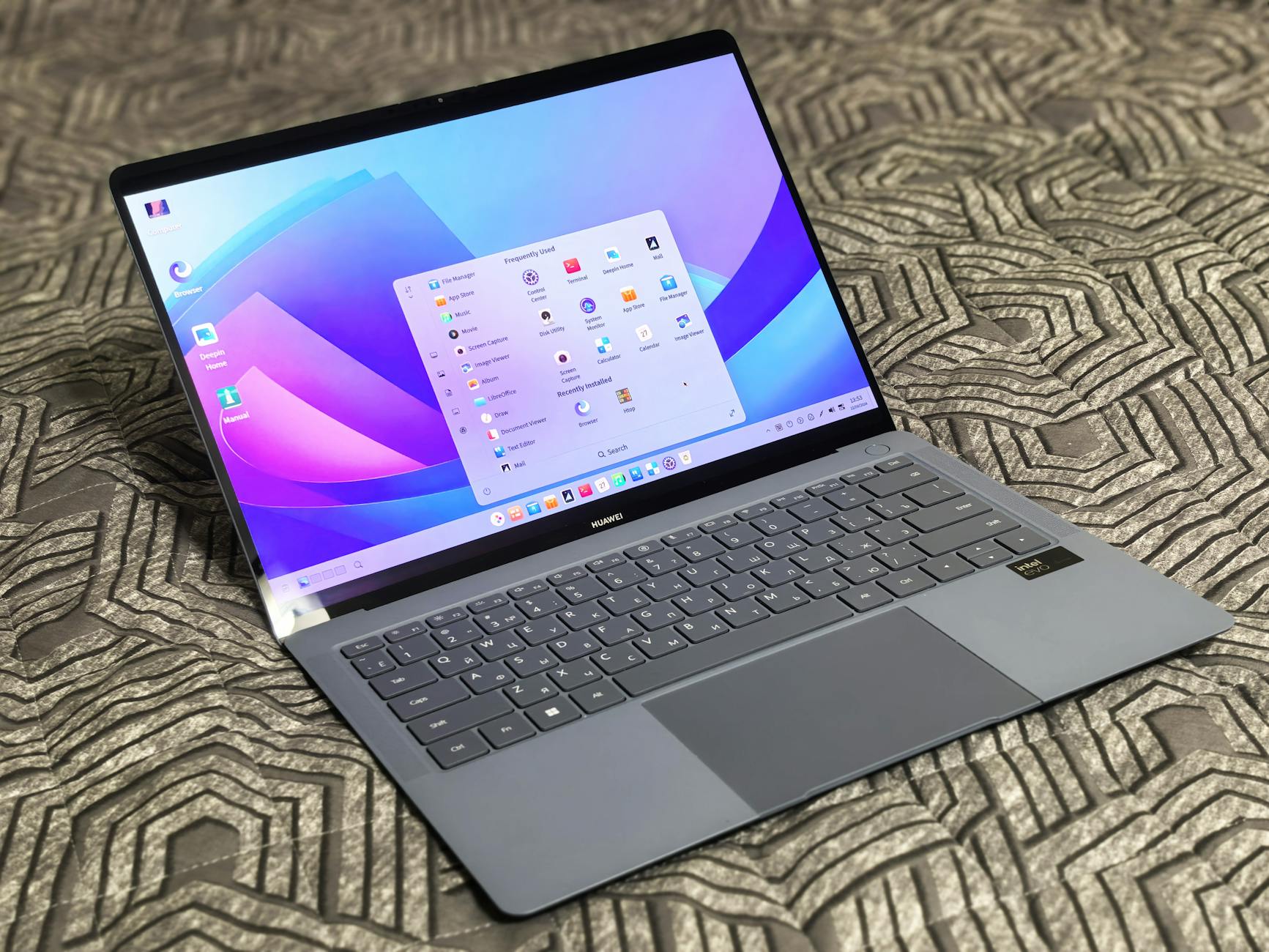 A sleek modern laptop with an open application menu on a patterned surface.