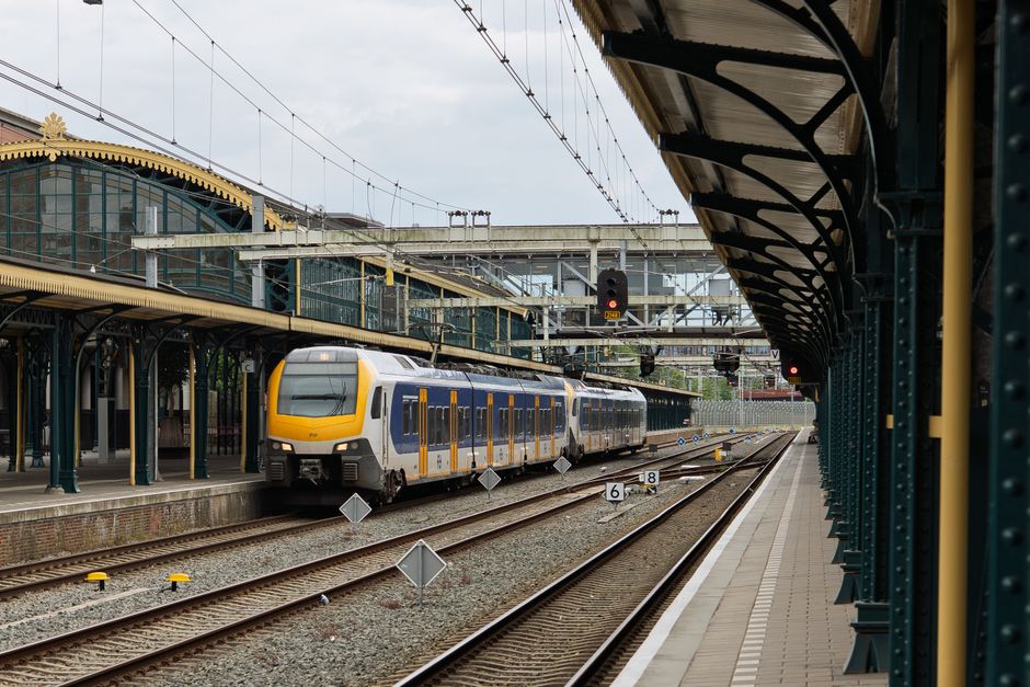 Modern train at a historic station with ironwork and glass architecture.