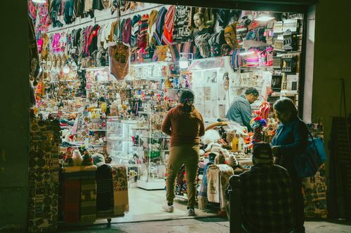 Free Vibrant night market stall filled with textiles and gifts, attracting customers of all ages and ethnicities. Stock Photo