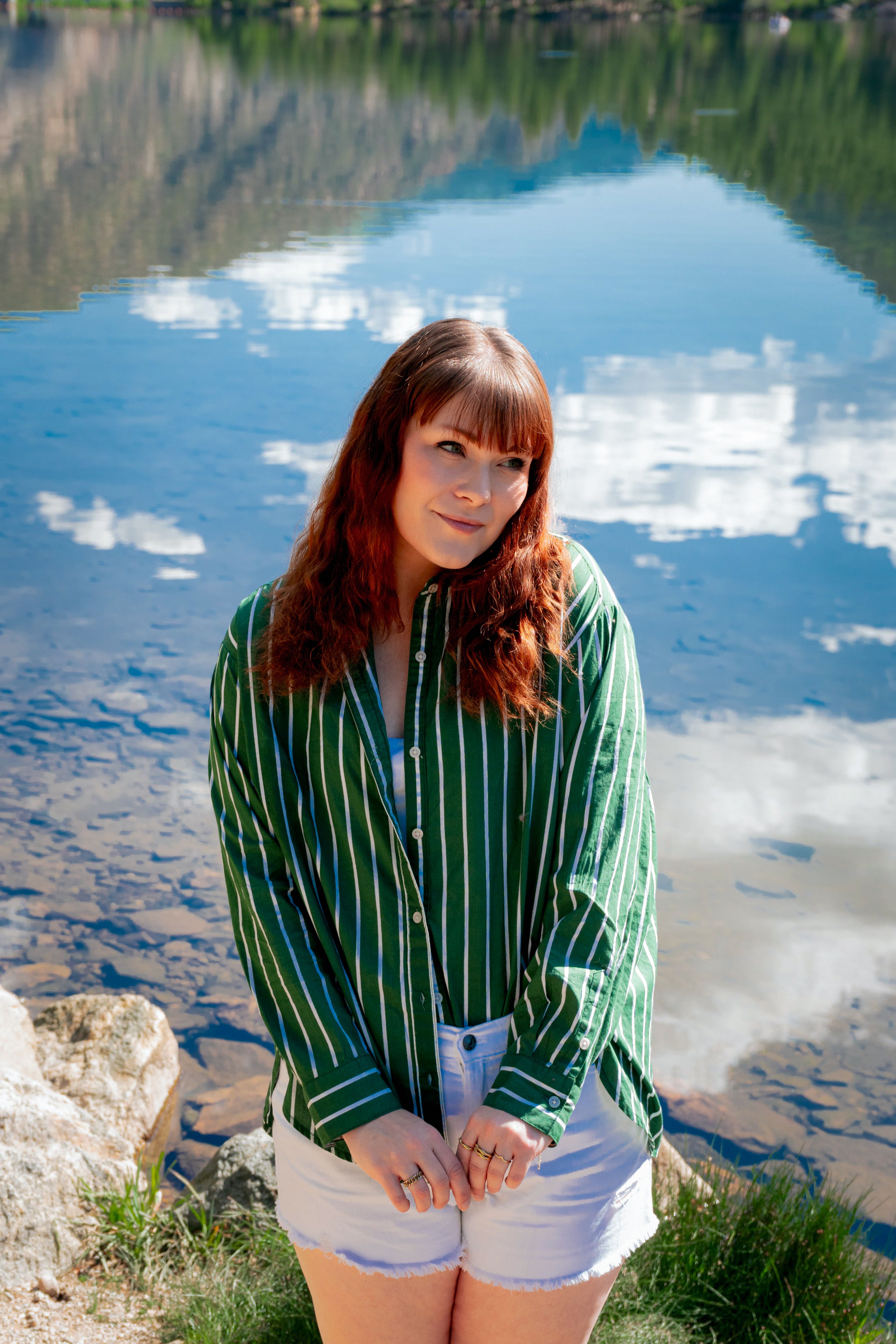 Young woman in green striped shirt poses by a reflective lake in Georgetown, Colorado, with mountains in the background.