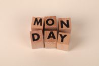Wooden blocks arranged to spell 'MONDAY' on a minimal beige background.