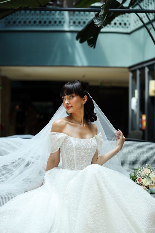 Free Beautiful bride in an elegant wedding dress sitting with floral bouquet, indoors. Stock Photo