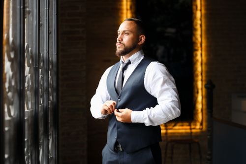 Free A man in a formal suit looks out the window while adjusting his vest, exuding confidence indoors. Stock Photo