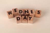 Wooden blocks arranged to spell Wednesday on a plain beige background, ideal for calendar or weekday concepts.