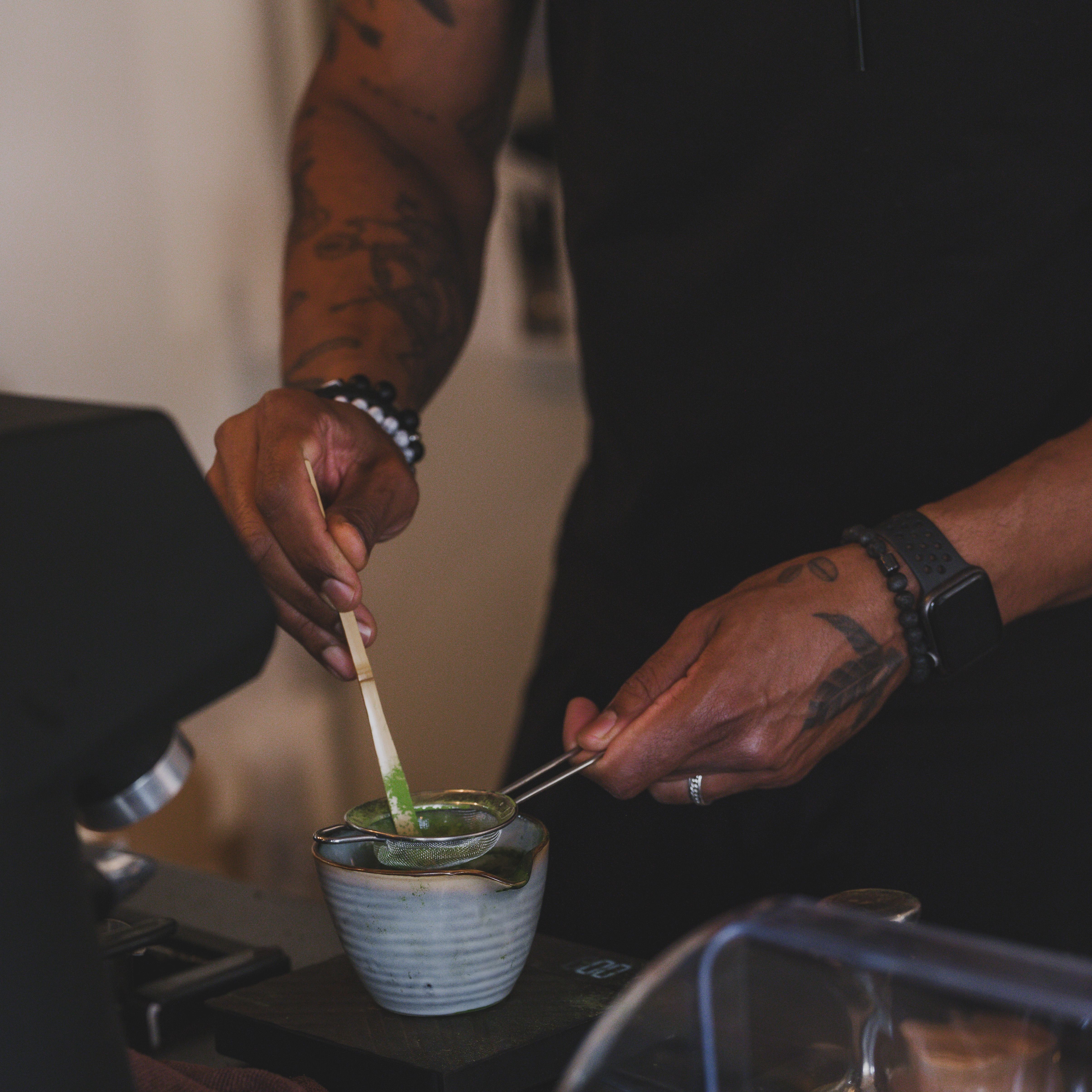 Tattooed barista skillfully preparing an iced matcha latte, highlighting craft and precision.