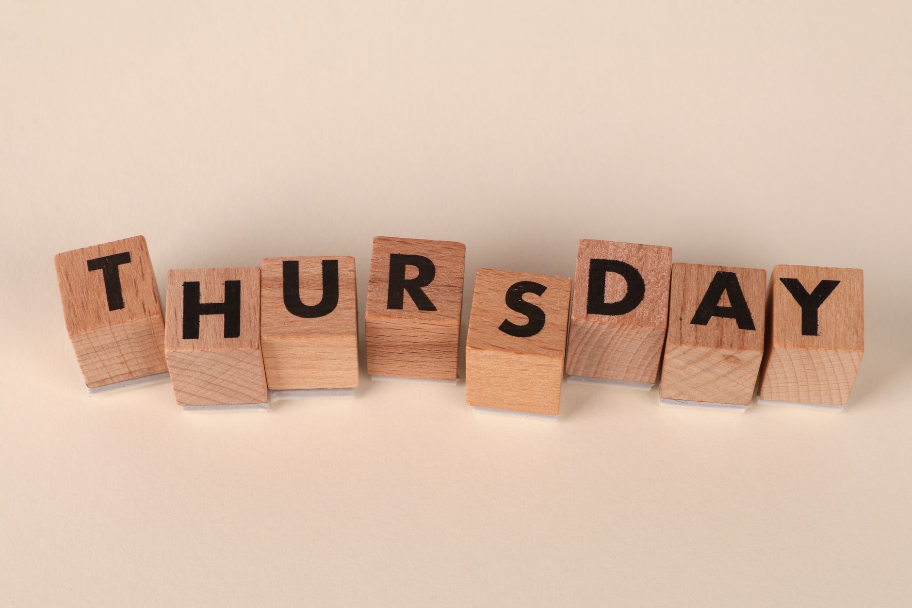 Wooden blocks arranged to spell Thursday on a neutral background.