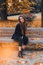 一位留着长发的时尚女子在落满秋叶的长凳上摆着姿势