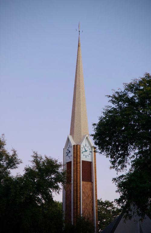 Free A prominent church steeple framed by trees under a sunset sky, showcasing architectural elegance. Stock Photo