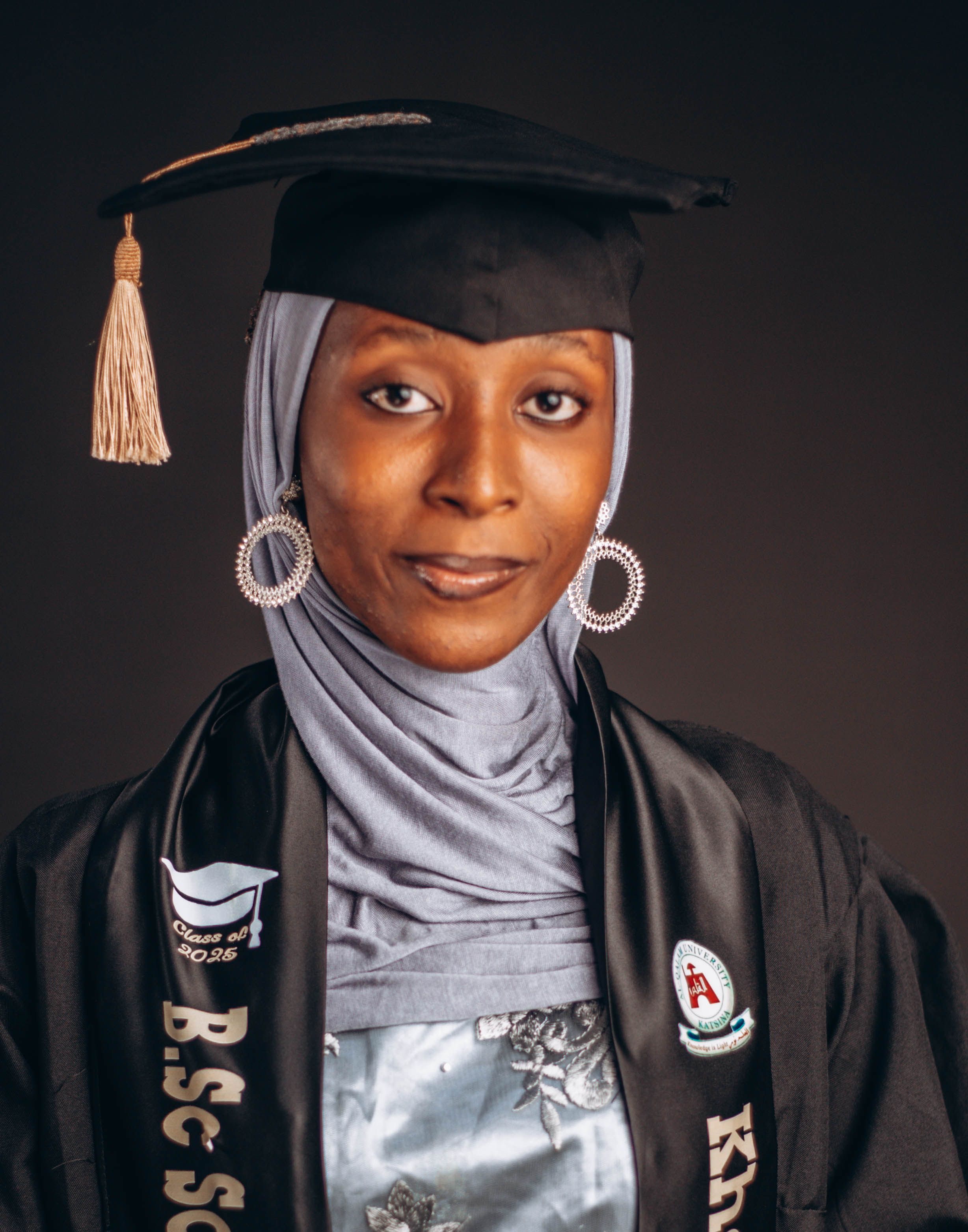 A young woman wearing a hijab and graduation gown, celebrating her academic achievement.