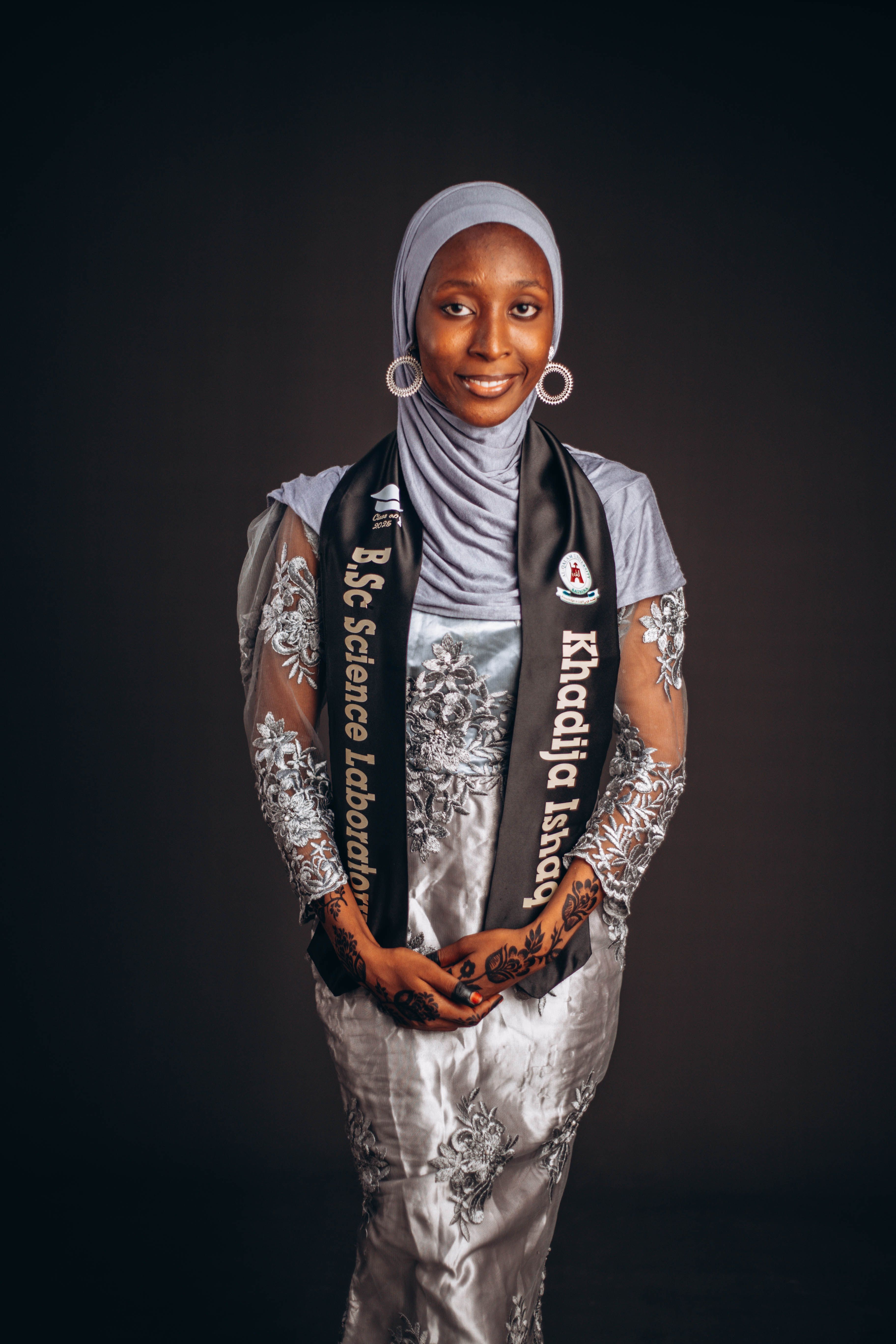 Smiling woman in formal attire and hijab celebrates graduation with a sash.