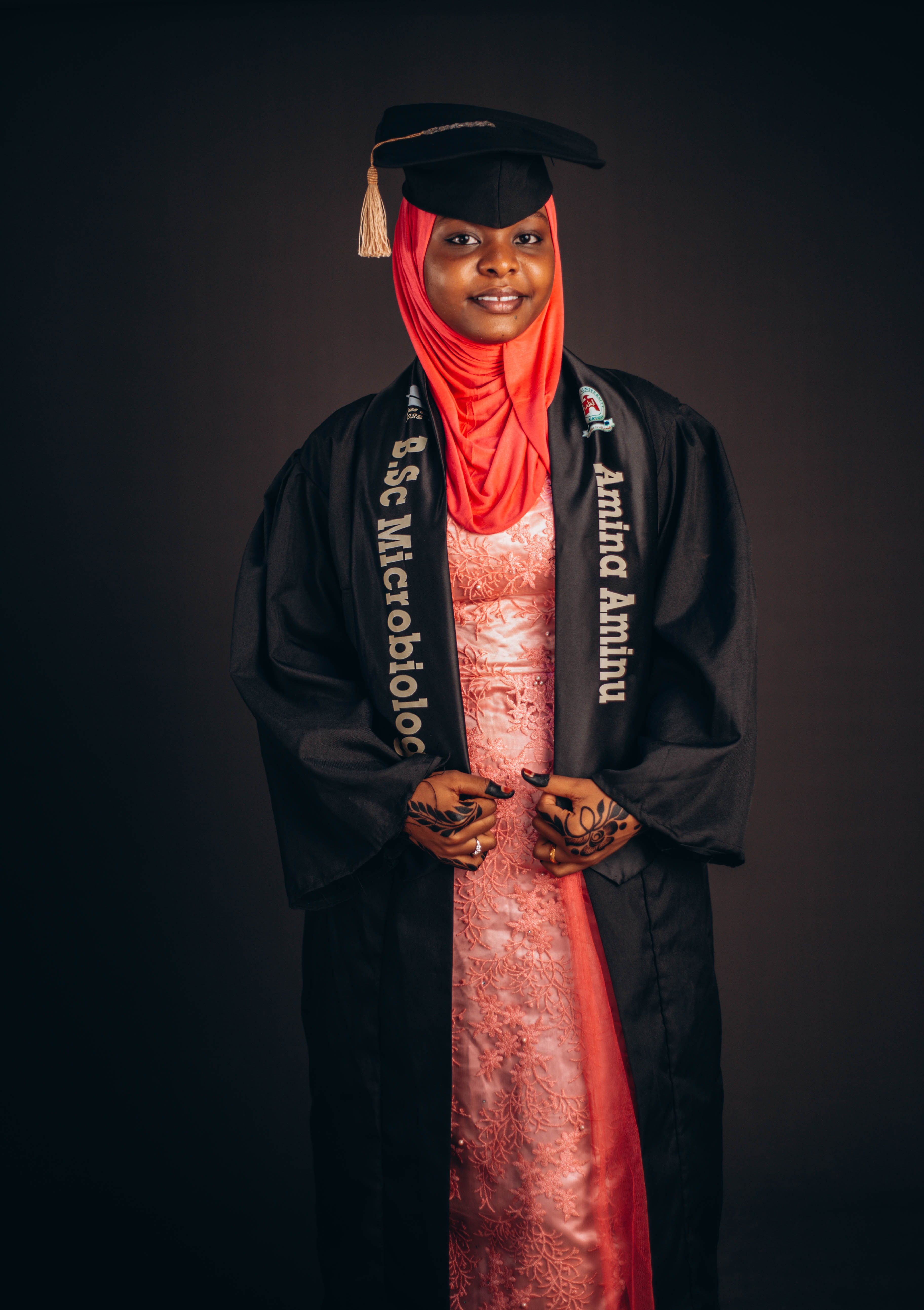 Proud graduate wearing cap, gown, and hijab posing with a smile.