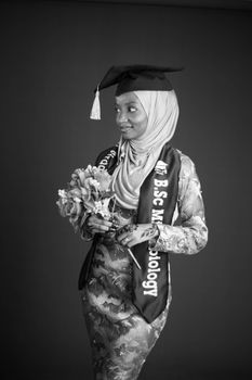 Elegant black and white portrait of a woman in hijab holding a bouquet, celebrating graduation.