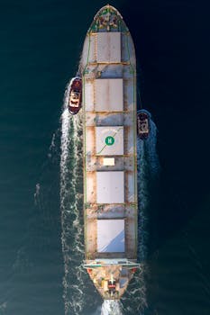 An aerial photo of a large cargo ship with tugboats assisting in open sea, showing maritime transportation.