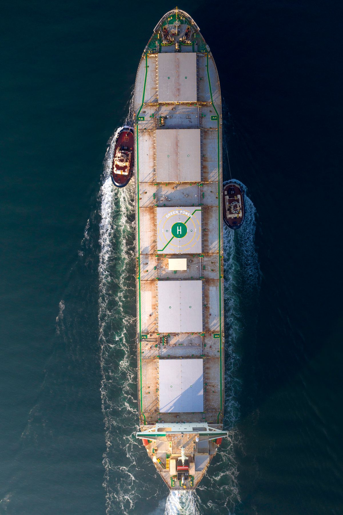 Aerial view of a cargo ship with tugboats at sea