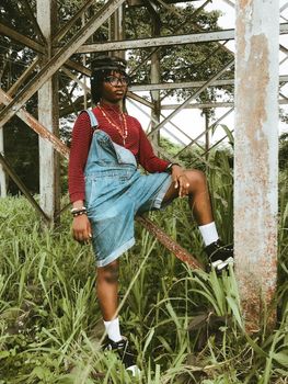A fashionable person posing confidently outdoors in denim overalls and stripes.