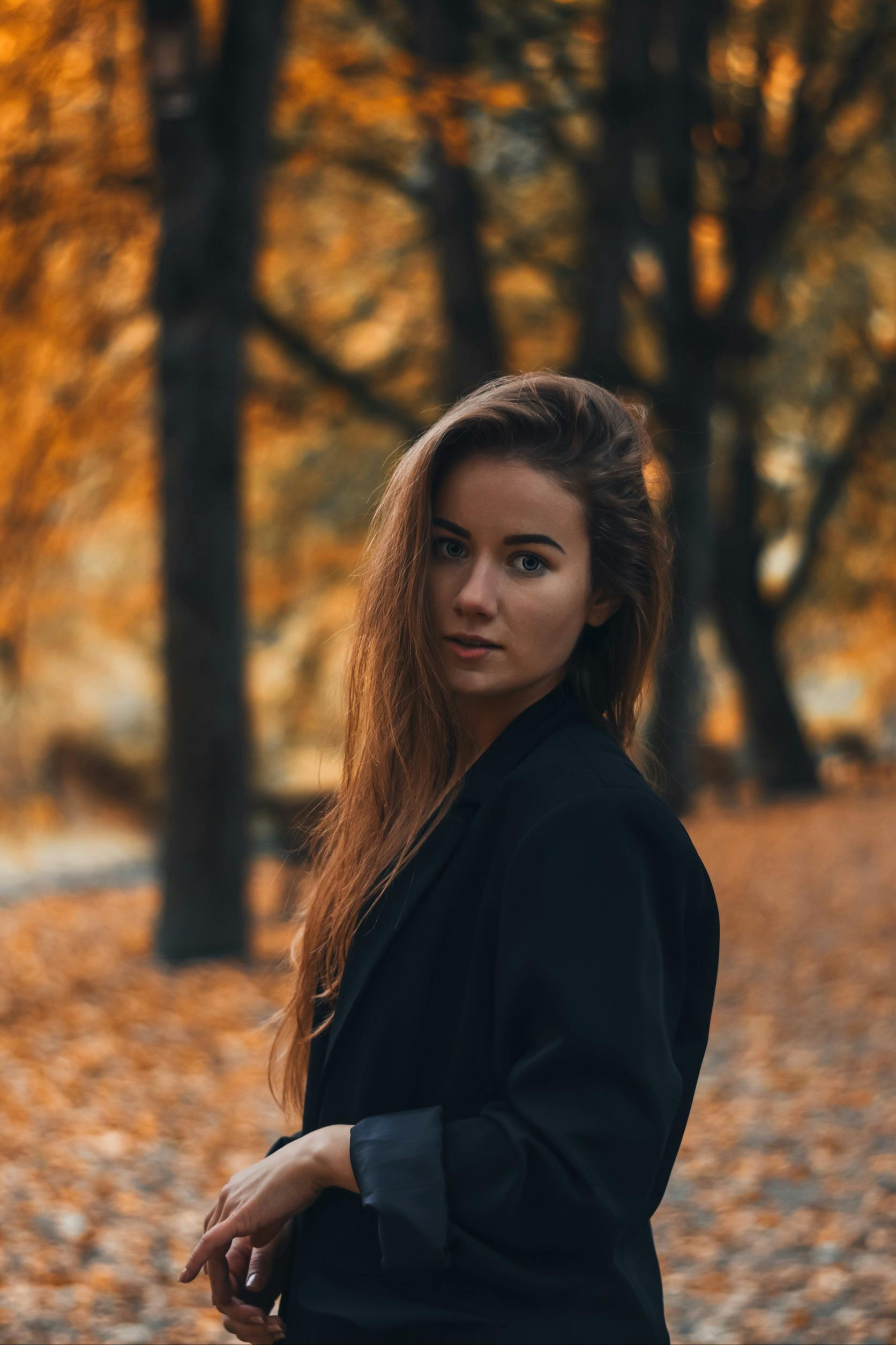 一位女子肖像立于宁静的秋林之中，色调温暖，灯光柔和