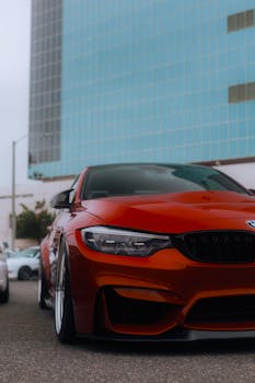 A vibrant orange car parked in front of a modern skyscraper in a city setting, showcasing urban elegance.