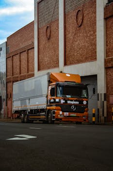 A large orange truck parked beside a brick industrial building in Mbabane, Eswatini.