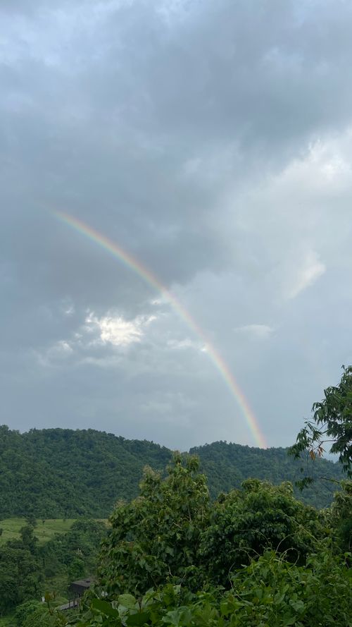 Free A beautiful rainbow arches over lush green hills under a cloudy sky, showcasing nature's beauty. Stock Photo