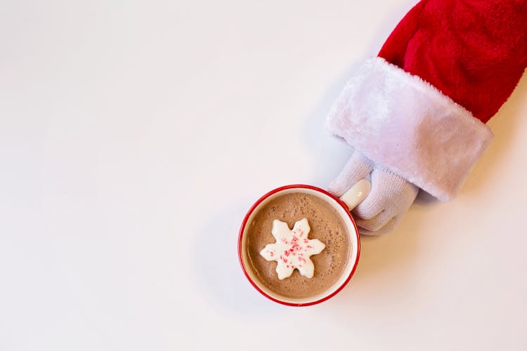 Mug Of Chocolate Drink With Snowflake-Shaped Cookie On Top Held By A Person In Santa Suit