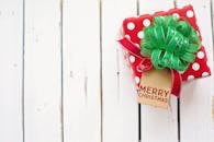 白色木制背景上，特写着带有绿色蝴蝶结和圣诞快乐标签的节日礼物