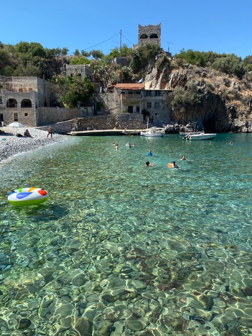 Free Swimmers enjoying a sunny day by Mani Peninsula's crystal waters and rustic architecture. Stock Photo