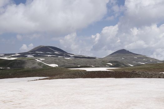 Stunning view of snow-capped mountains under a bright sky with fluffy clouds.