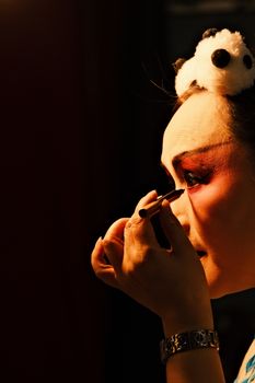 Close-up of person applying makeup in dim theater setting with panda headpin.