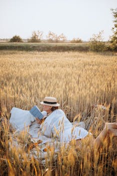 A woman enjoying a book in a peaceful wheat field setting during the day.