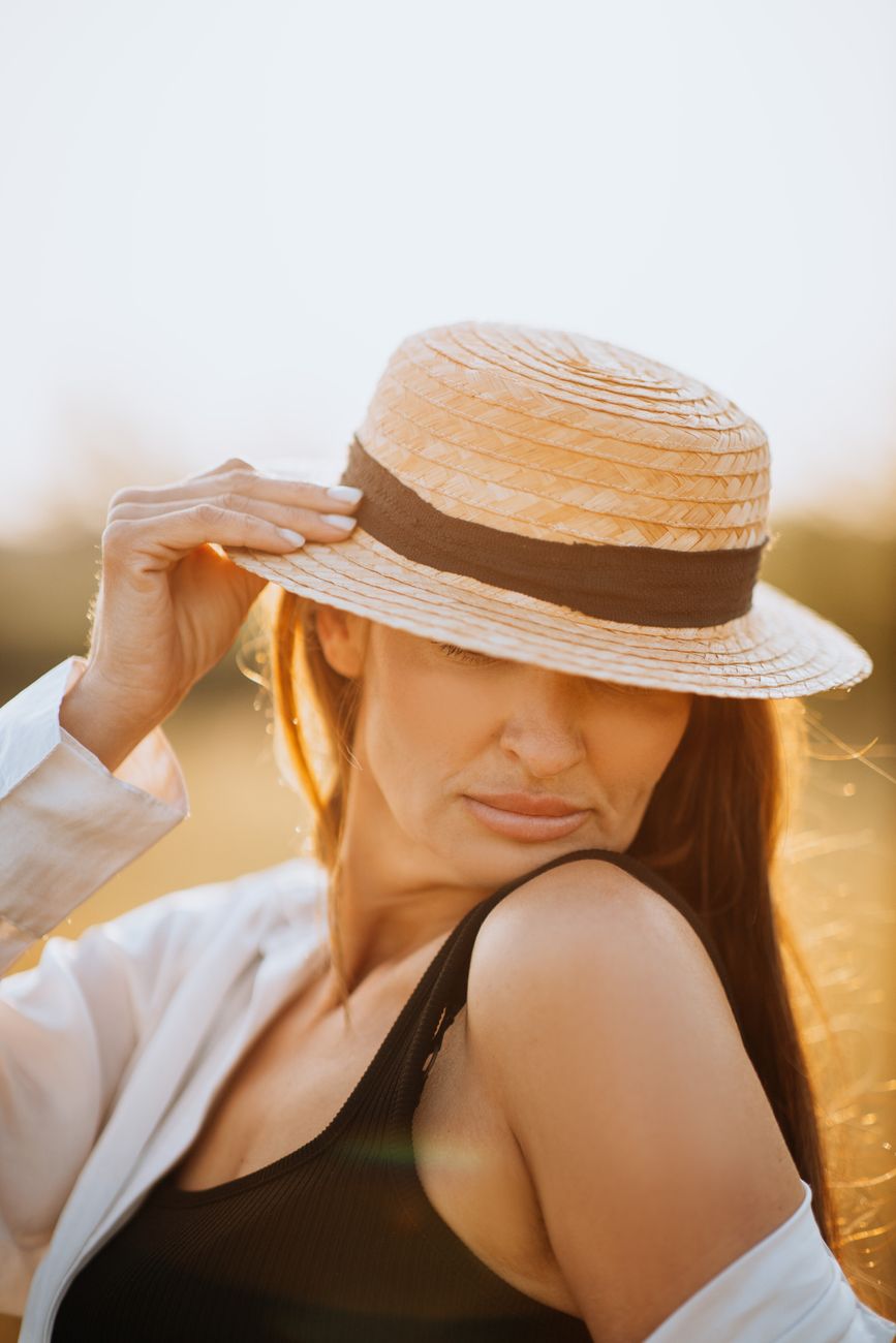 A stylish woman wearing a straw hat enjoys the golden sunlight outdoors