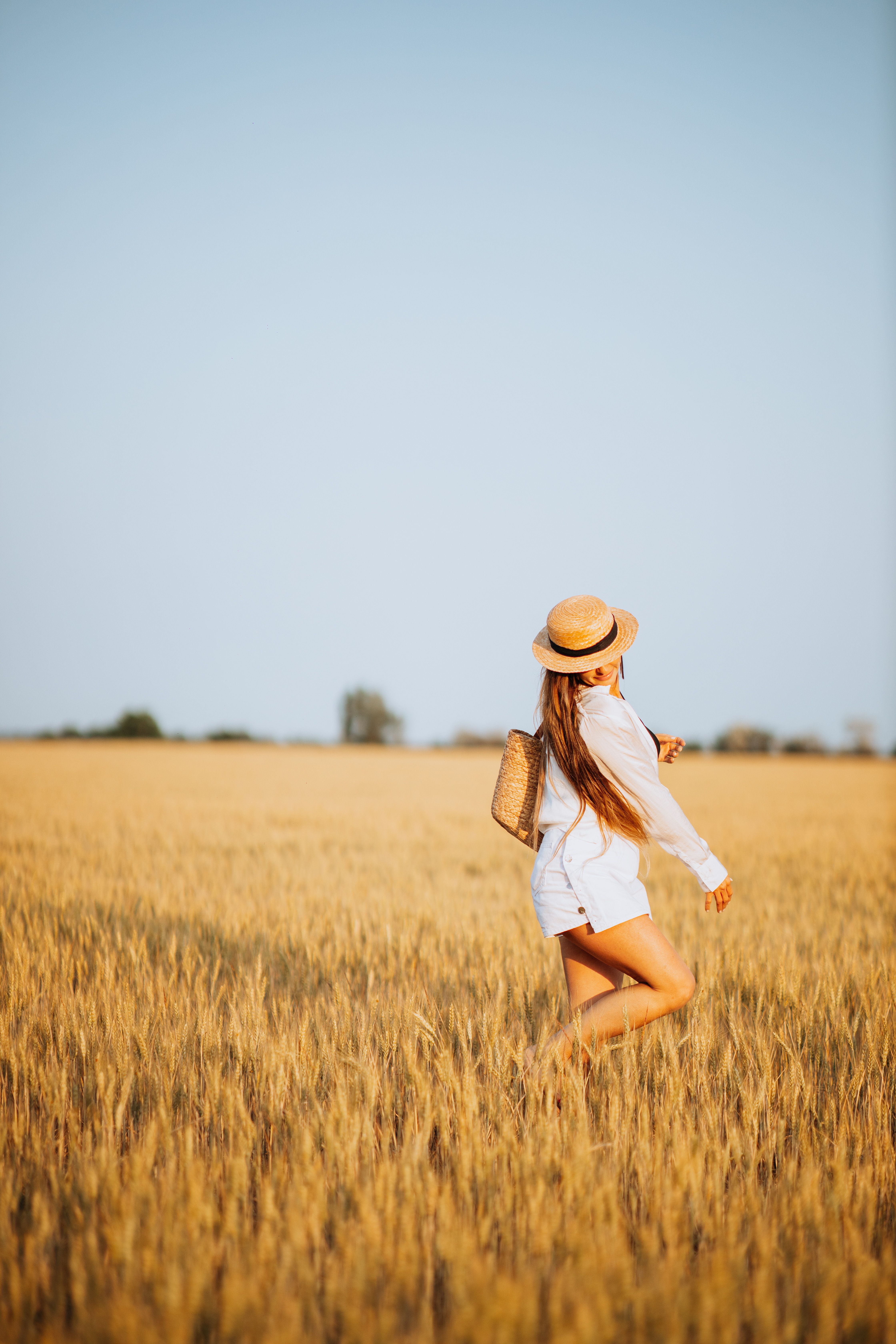 A carefree woman in a hat walks through a sunlit golden wheat field, embodying summer freedom.