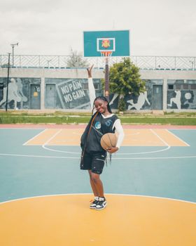 Confident teen girl poses on an outdoor basketball court with a ball.