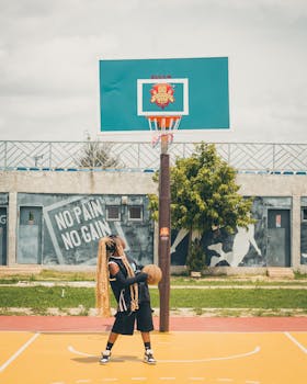 Teen basketball player with long braids holding a ball on a sunny outdoor court.