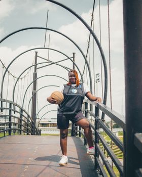 Confident young athlete holding a basketball on an arched urban bridge, cityscape background.