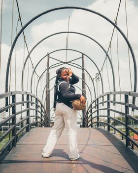 Confident woman with braided hair posing on an industrial bridge under a bright sky.