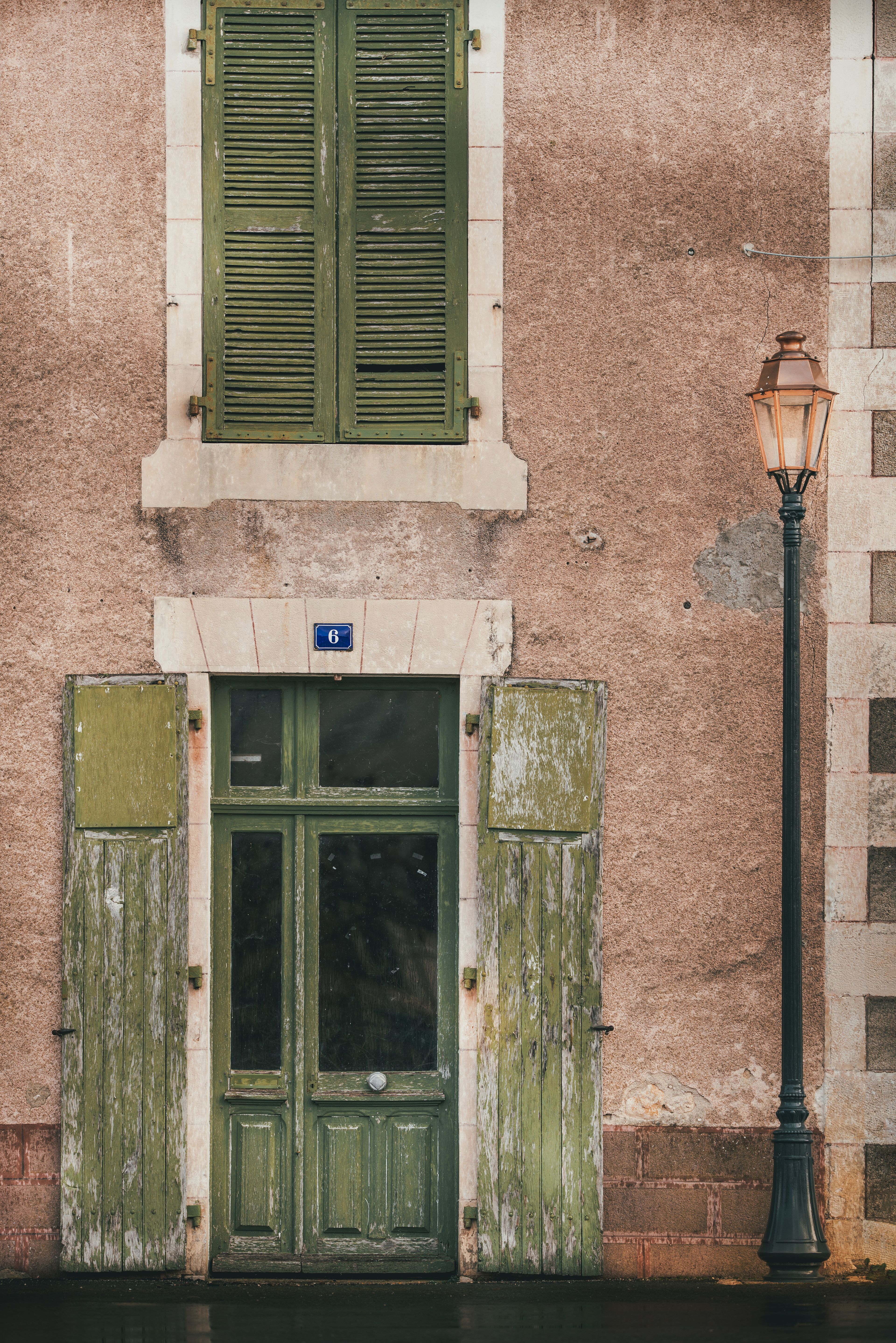 Porte en bois et volets d'une maison de ville française, façade claire, lumière d'après-midi.