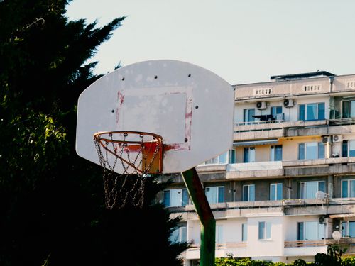 Free An outdoor basketball hoop stands in front of apartment buildings and trees under a clear sky. Stock Photo