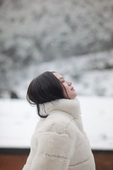 Side view of a young woman in a fur coat enjoying a snowy winter landscape.