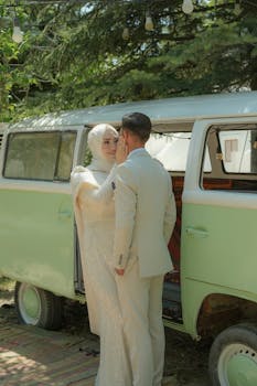 A couple in elegant attire sharing a moment outdoors beside a vintage van.