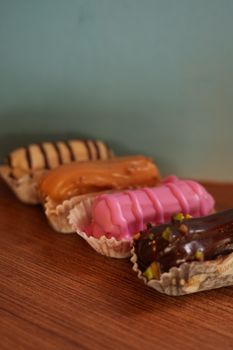 Four vibrant eclairs in a row on a wooden surface with a pastel backdrop, offering a delectable treat for dessert lovers.