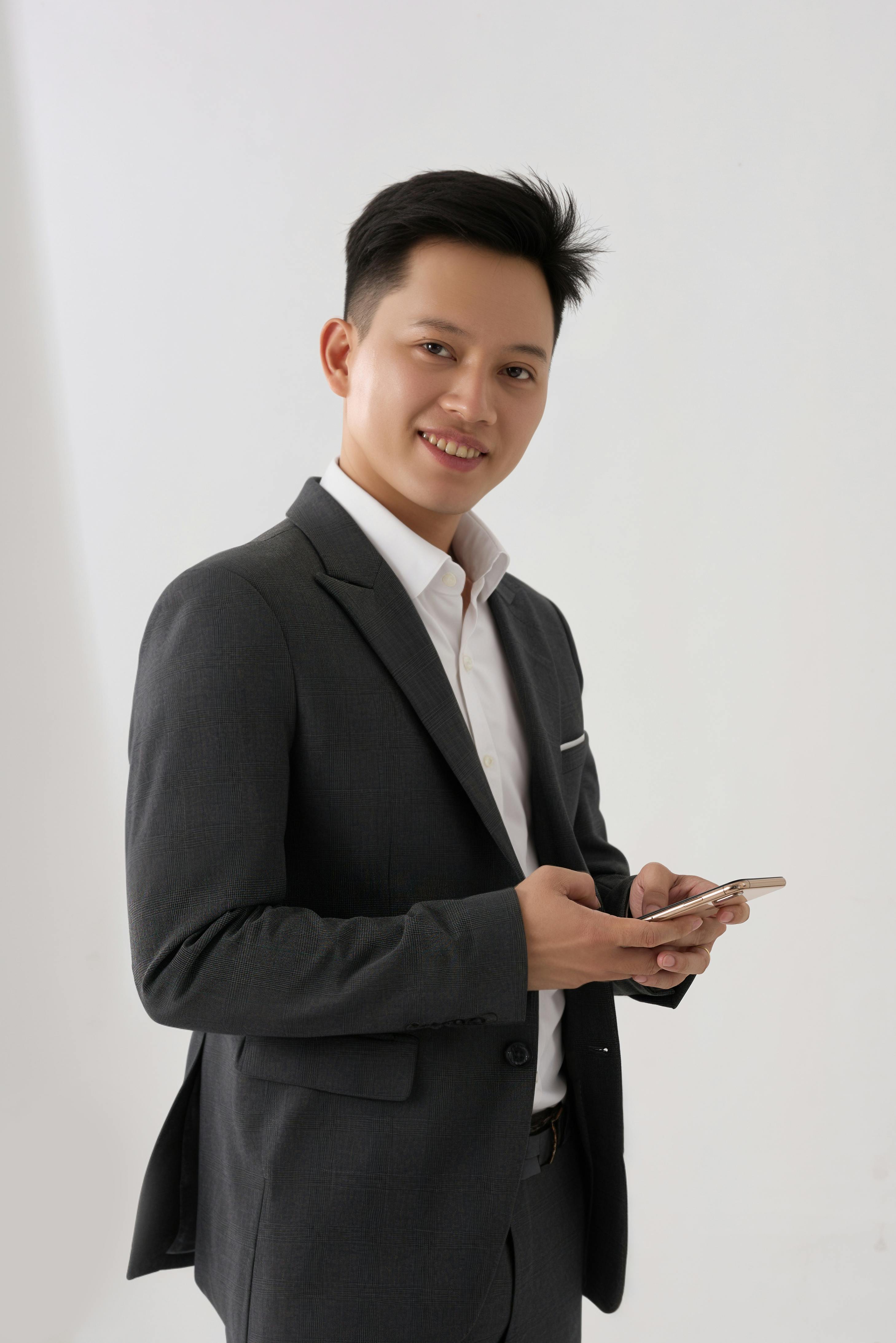 bezplatná Portrét sebevědomého dospělého muže v obleku, který drží chytrý telefon a usmívá se. Základová fotografie