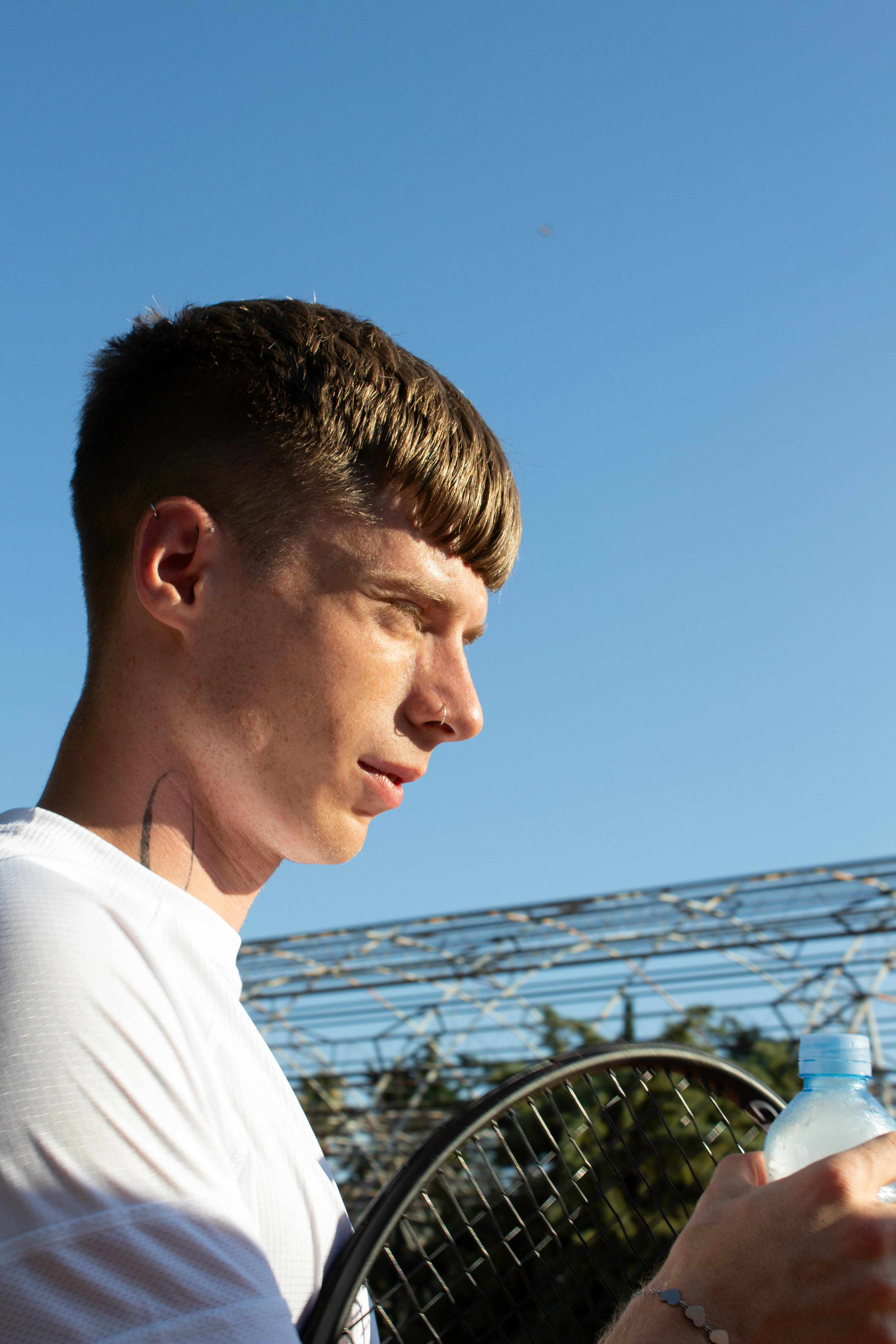 Side profile of a male tennis player in Budva, Montenegro, holding a racket and water bottle.
