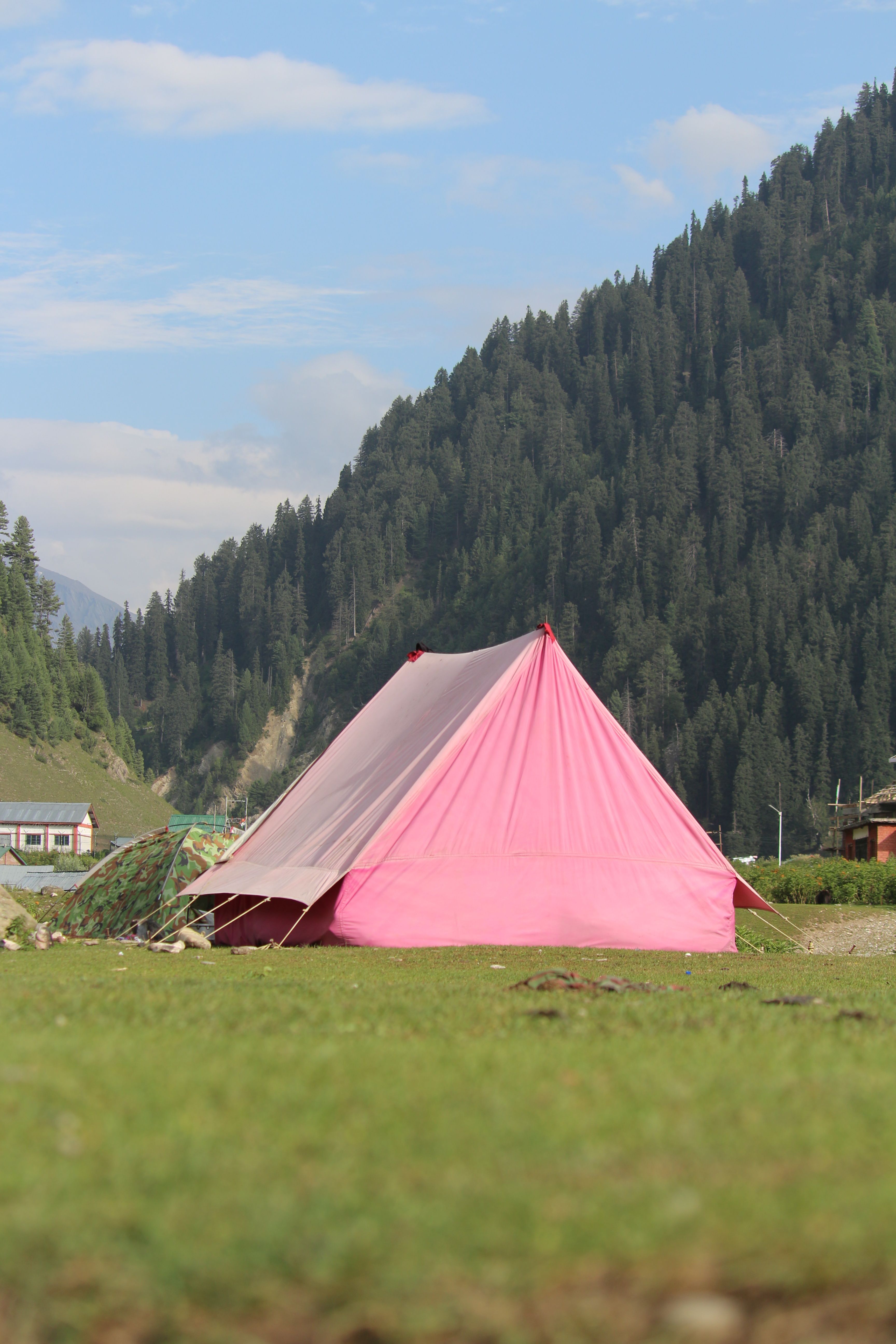 A vibrant pink tent set against a lush mountain backdrop under a clear blue sky.